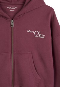 Burgunderfarbene Zip-Hoodie aus Bio-Baumwolle, mit einer Vordertasche und weißen bestickten Logodetails auf der Brust.