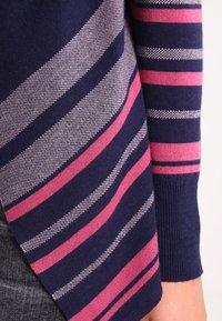 Námořnický modrý pletený svetr s vodorovnými pruhy v růžové a světle šedé barvě, s žebrovanými manžetami a měkkou texturou.