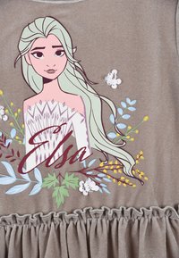 Grauer Stoff-Oberteil mit Rüschensaum. Mit einem großen, bunten Grafikdesign eines Charakters mit hellgrünen Haaren, floralen Akzenten und dem Namen "Elsa".