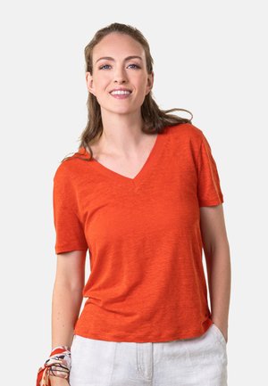 Kurzärmliges, V-Ausschnitt T-Shirt in leuchtendem Orange, aus strukturiertem Gewebe. Kombiniert mit hellen, lässig geschnittenen Hosen.