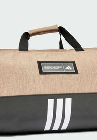 Torba sa duffle stilom s teksturiranim svijetlosmeđim tijelom, crnim detaljima i bijelim prugama. Ima čvrstu crnu ručku i oznaku branda.