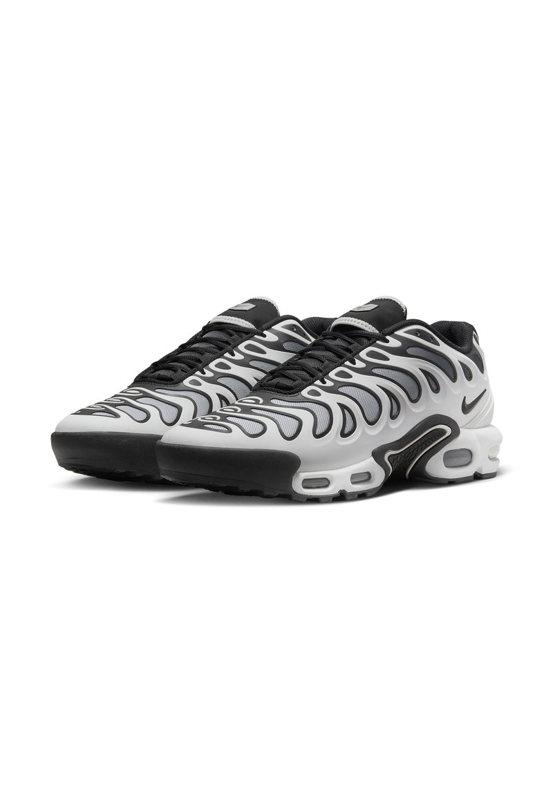Chaussures de sport noires et blanches avec un design ondulé, tige en mesh, fermeture à lacets, col rembourré et amorti d'air visible dans la semelle.