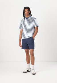Stribet kortærmet skjorte i hvid og blå, parret med navy shorts. Båret med hvide sneakers med sorte detaljer og ribbede sokker.