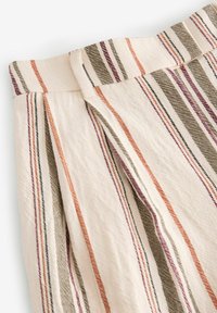 Tissu rayé en coton crème, avec des lignes verticales dans des teintes d'orange, de vert et de bordeaux. Détail de taille plissée visible.