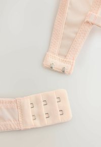 Fermeture de bretelle de soutien-gorge rose clair avec trois crochets métalliques d'un côté et deux œillets métalliques de l'autre, sur un fond clair uni.