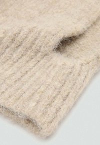 Béžová pletená tkanina s jemnou textúrou, s rebrovaným vzorom a voľnými vláknami. Tvar je na spodnom okraji preložený.