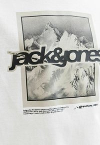 Zwart-witte bergtoppen met een groot "jack & jones" logo erbovenop, en kleine tekst over buiteninspiratie en een beperkte editie eronder.