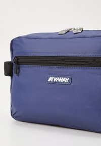 Tamno plavi platneni torba s teksturiranom površinom, s duplim srebrnim zatvaračem i K-Way logotipom. Ima prednji džep s crnim zatvaračem.