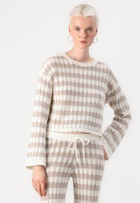 Pull en crochet beige et blanc cassé à rayures, avec un col rond, des manches amples et une coupe courte.
