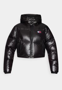 Veste matelassée courte noire brillante avec capuche, fermeture éclair à l'avant, poches biseautées et logo Tommy Jeans sur la poitrine.