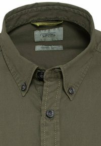 Chemise boutonnée vert olive avec un col structuré, des surpiqûres contrastantes et des boutons foncés. Comprend une étiquette teinte en pièce à l'intérieur.