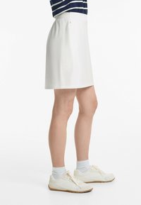 Jupe blanche de longueur genou avec une taille élastique et une poche latérale, associée à des baskets blanches et des chaussettes rayées bleu clair.