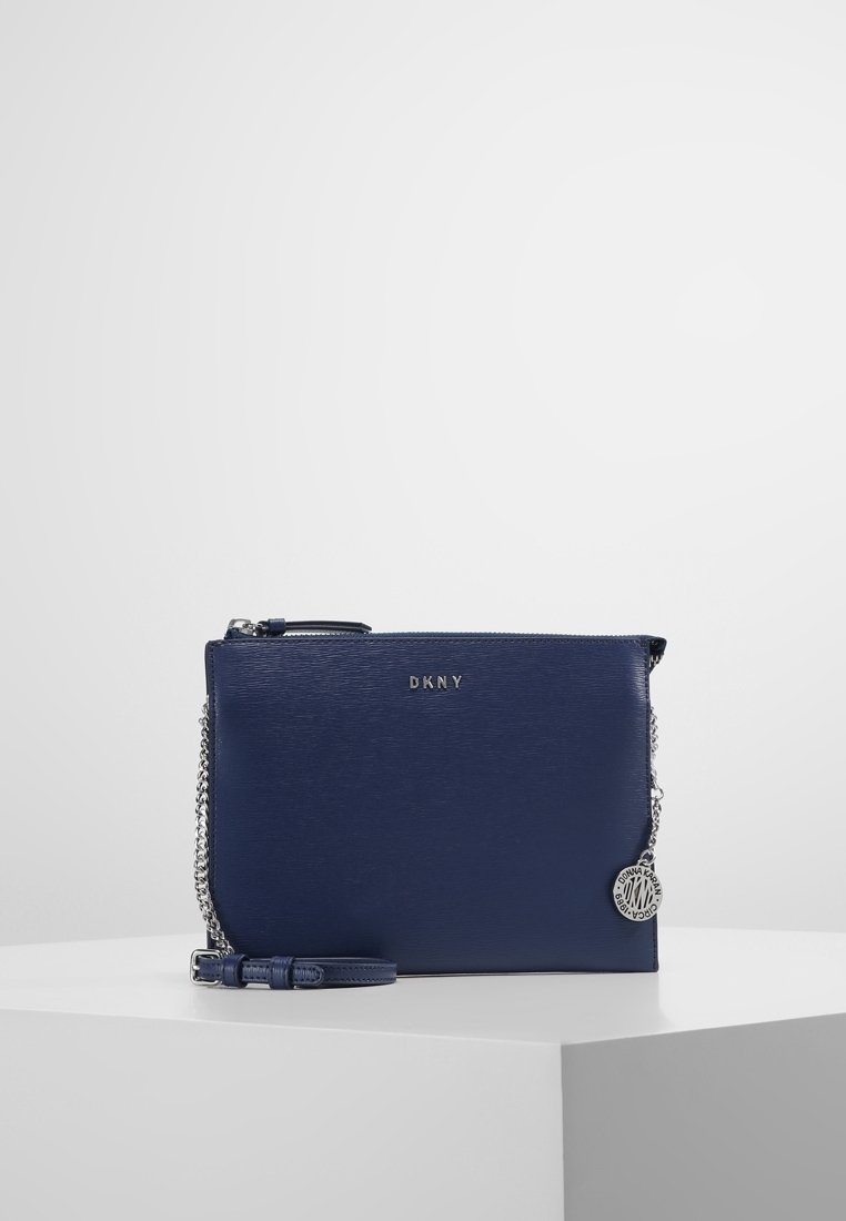 Granatowa torba na ramię DKNY z fakturowanym wykończeniem, srebrnym łańcuszkiem, logo z przodu i odpinanym ozdobnym breloczkiem. Zapięcie na zamek.