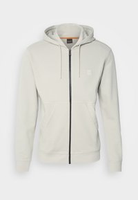 Felpa zip grigia chiara realizzata in tessuto morbido, con zip nera, due tasche frontali e cappuccio. Nessun motivo o accento visibile.