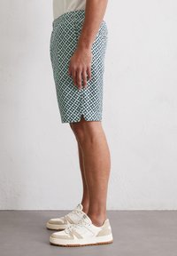 Men’s patterned shorts in green and white with star motifs. Constructed from lightweight material, featuring a straight cut and side slits.