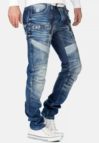 Jeans in denim con un lavaggio blu medio e una vestibilità affusolata, caratterizzati da dettagli cuciti, molteplici tasche e una superficie liscia.