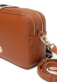 Borsa a tracolla in pelle marrone con texture, zip dorate, tracolla removibile e un dettaglio hardware brandizzato. Forma rettangolare, design minimalista.