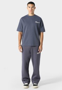 Mørkegrå bomulds T-shirt med korte ærmer og rund hals, parret med matchende sweatpants med et logo-patch på siden. Sorte sneakers.