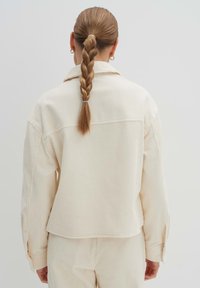 Cremfarbener gerippter Cord-Hemd mit lockerer Passform, tief sitzenden Schultern und spitzem Kragen. Passt gut zu Hosen mit ähnlicher Textur.