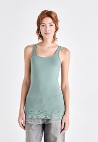 Mintgrønn tanktop med en tettsittende design, med blonderkant nederst. Stoffet er glatt, med brede stropper og utringning.