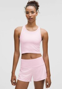 Helles Pink Sportset mit einem verkürzten Tanktop mit feiner Rippstruktur und passenden hochgeschnittenen Shorts. Glatte Stoffoberfläche.