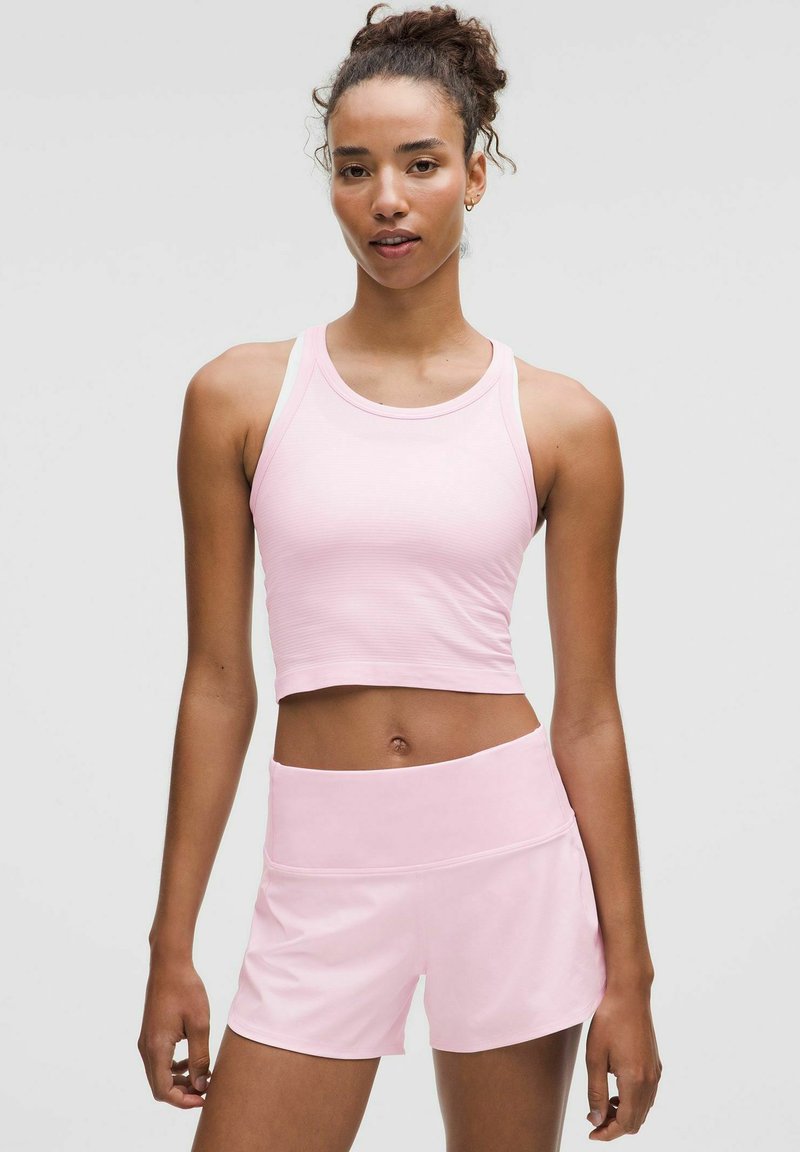 Helles Pink Sportset mit einem verkürzten Tanktop mit feiner Rippstruktur und passenden hochgeschnittenen Shorts. Glatte Stoffoberfläche.