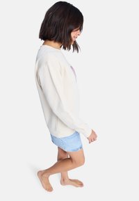 Sudadera de crema clara con un corte relajado, cuello redondo y puños acanalados, combinada con una falda de mezclilla azul clara. Sin patrones visibles.