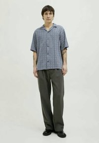 Chemise à manches courtes avec boutons de couleur bleue, ornée d'un motif à losanges, assortie à un pantalon large gris et des chaussures noires.