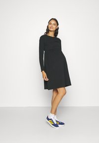 Czarna sukienka z długim rękawem, dopasowaną górą i rozkloszowanym dołem. Noszona z niebieskimi trampkami z żółtymi paskami i białymi podeszwami.