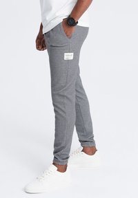 Pantalones de chándal grises con un patrón texturizado, diseño ajustado, puños elásticos, bolsillos laterales y una etiqueta en el bolsillo trasero. Combinados con zapatillas blancas.
