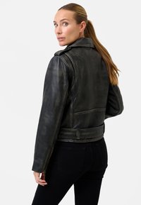 Svart läderjacka med vintagefinish, med krage, dragkedja och två sidofickor; bärs tillsammans med svarta jeans.