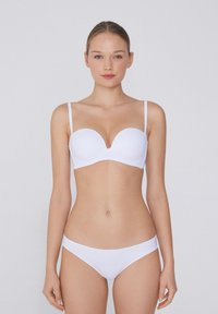 Bílá vycpaná podprsenka s hlubokým výstřihem a tenkými nastavitelnými ramínky, spárovaná s odpovídajícími bílými bikinovými kalhotkami, hladká látka.