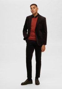 Svart sammetblazer över en röd tröja, i kombination med mörka byxor och bruna loafers. Ensemblet har skräddarsydda passformer och en stilren design.