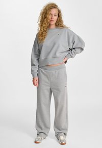 Graues, kurz geschnittenes Sweatshirt mit langen Ärmeln und Logodetails, kombiniert mit locker sitzenden grauen Sweatpants und silbernen Sneakern.