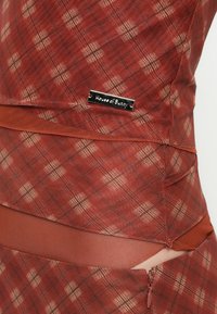 Checkered red dress with a textured fabric. Features a subtle plaid pattern, a zipper detail, and a metallic brand tag on the side.