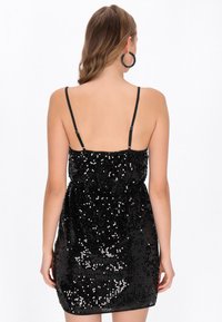 Fekete flitteres ruha vékony pántokkal, testhezálló felsőrésszel és rövid szegéllyel, sima textúrával és fényes felülettel.