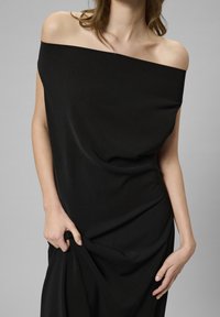 Svart off-the-shoulder klänning med draperad design och slät textur. Tyget har en subtil lyster och en avslappnad silhuett.