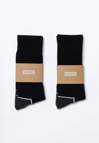 Czarno-szare skarpetki prążkowane z białym akcentem, oznaczone napisem "SNOCKS WORKING SOCKS", zapakowane razem z brązowym kartonowym paskiem.