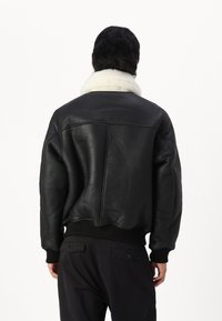 Černá kožená bomber bunda s bílým ovčím límcem, žebrovanými manžetami a lemem. Má hladký texturovaný povrch a ležérní design.