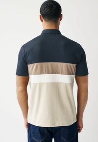 Polo majica z mornarsko modrim zgornjim delom, svetlo rjavimi, belimi in bež vodoravnimi črtami. Narejena iz mehke tkanine, s kratkimi rokavi in klasičnim ovratnikom.