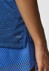 Modrá sportovní blůza z texturované látky s logem "climalite" v kombinaci s modrou perforovanou sukní, která ukazuje ventilační detaily.