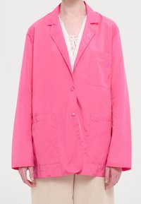 Veste légère rose à coupe décontractée, fermeture à un bouton, deux poches avant et revers crantés. Texture lisse, détails minimaux.