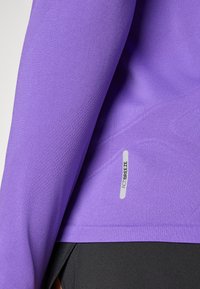 Purple athletic long-sleeve shirt with smooth texture, slim fit, and "ACTIBREEZE" tag. Features breathable fabric with seamless stitching detail.