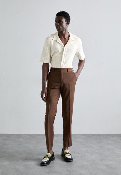 Witte shirt met korte mouwen en een gemêleerd patroon, bruine op maat gemaakte broek en zwarte instappers met een kleurrijke accenten. Eenvoudige, moderne pasvorm.