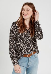 Chemise noire à boutons avec un motif léopard en crème et beige, manches longues et coupe décontractée, associée à un jean bleu clair et une ceinture marron.