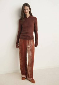 Bordo dukserica s dugim rukavima i prednjim zatvaračem, uparuena sa širokim, dvobojnim baršunastim hlačama u nijansama crvene i smeđe.