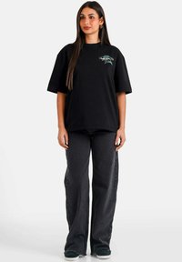 Camiseta negra de gran tamaño hecha de algodón con un estampado gráfico en el pecho, combinada con jeans negros acampanados y zapatos negros sin cordones.