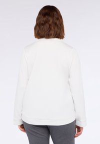 Felpa bianca con scollo rotondo, maniche lunghe, texture morbida e vestibilità rilassata, abbinata a pantaloni grigi. Nessun motivo o dettaglio visibile.