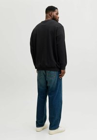 Sort sweatshirt med rund hals, ribstrikkede ærmekanter og taljebånd. Kombineret med lyseblå, afslappede denimjeans og hvide sneakers.