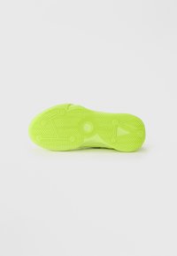 Lysende neon grøn sneaker sål med cirkulære og lineære dækmønstre på en ensfarvet lys grå baggrund.
